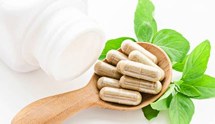 A spoonful of supplement capsules next to a white bottle and green leaves
